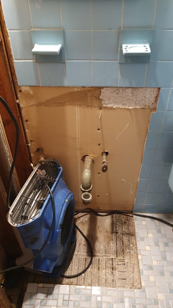 A bathroom with a section of wall removed and an air mover for water damage restoration by New Method Restoration in Edison, NJ.