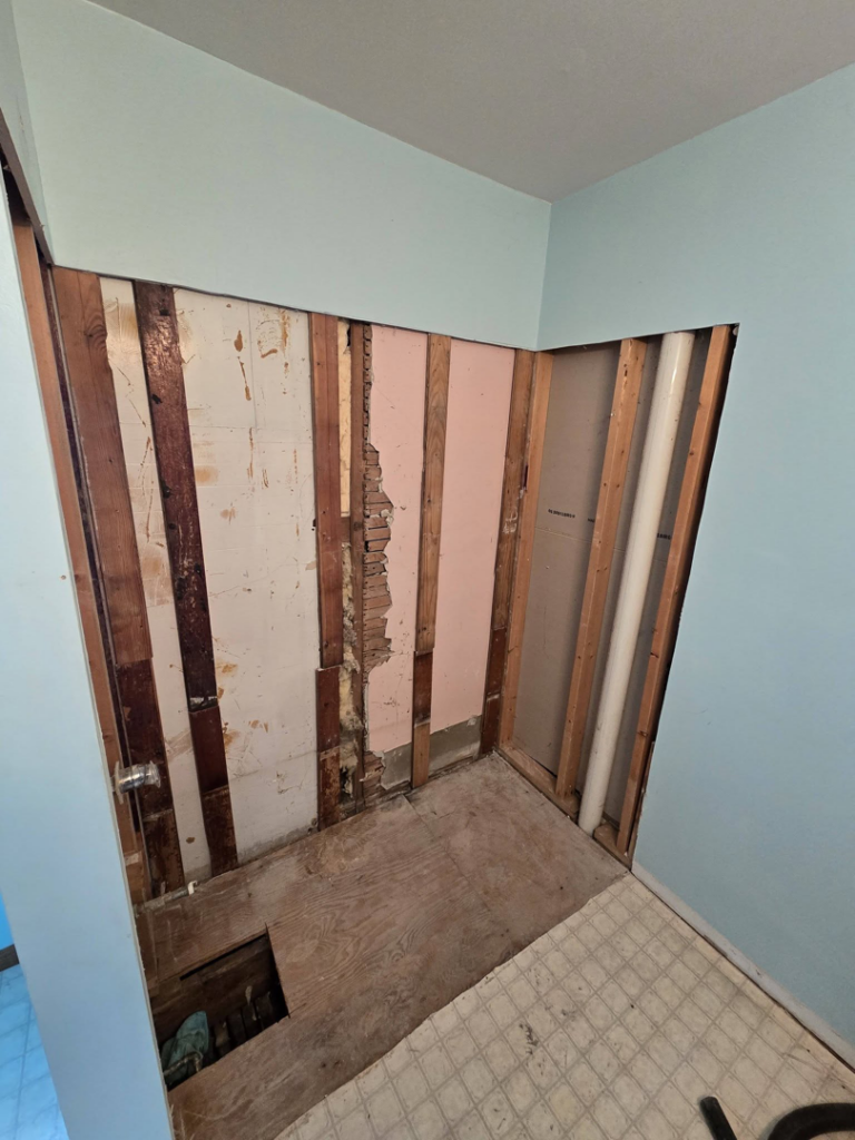 A bathroom wall with drywall removed, exposing wooden studs with visible water damage, by Katsma's Handyman Services LLC in Oshkosh, WI.