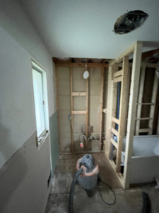 A bathroom undergoing water damage demolition with exposed studs and a shop vac by 24K Restoration in Flint, MI.