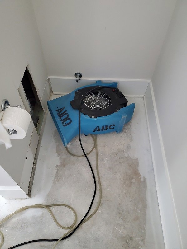 Water damage drying equipment, including an air mover, in a bathroom by ABC Cleaning and Restoration in Harvest, AL.