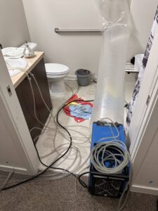 Water damage drying equipment, including an air mover and hoses, set up in a bathroom by The Recover Tech Restoration in Vancouver, WA.