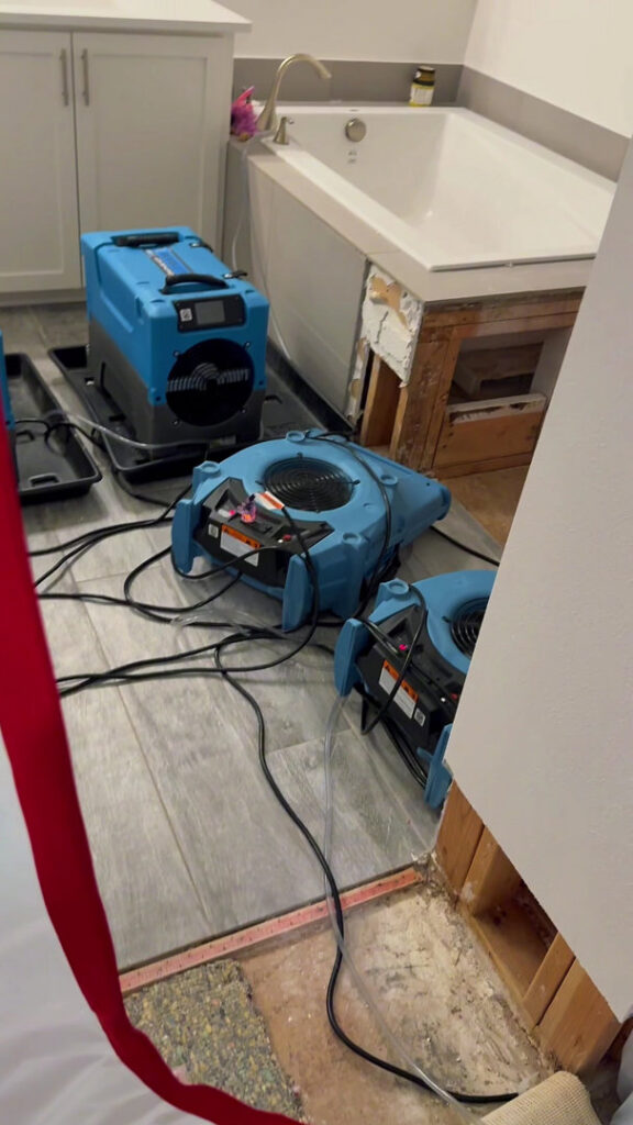 Water damage drying equipment in a bathroom with exposed subfloor and wall damage by Verg Restoration in Vancouver, WA