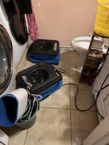 Industrial drying fans addressing water damage on a tiled bathroom floor near a washing machine by Prime Restoration in Lancaster, PA.