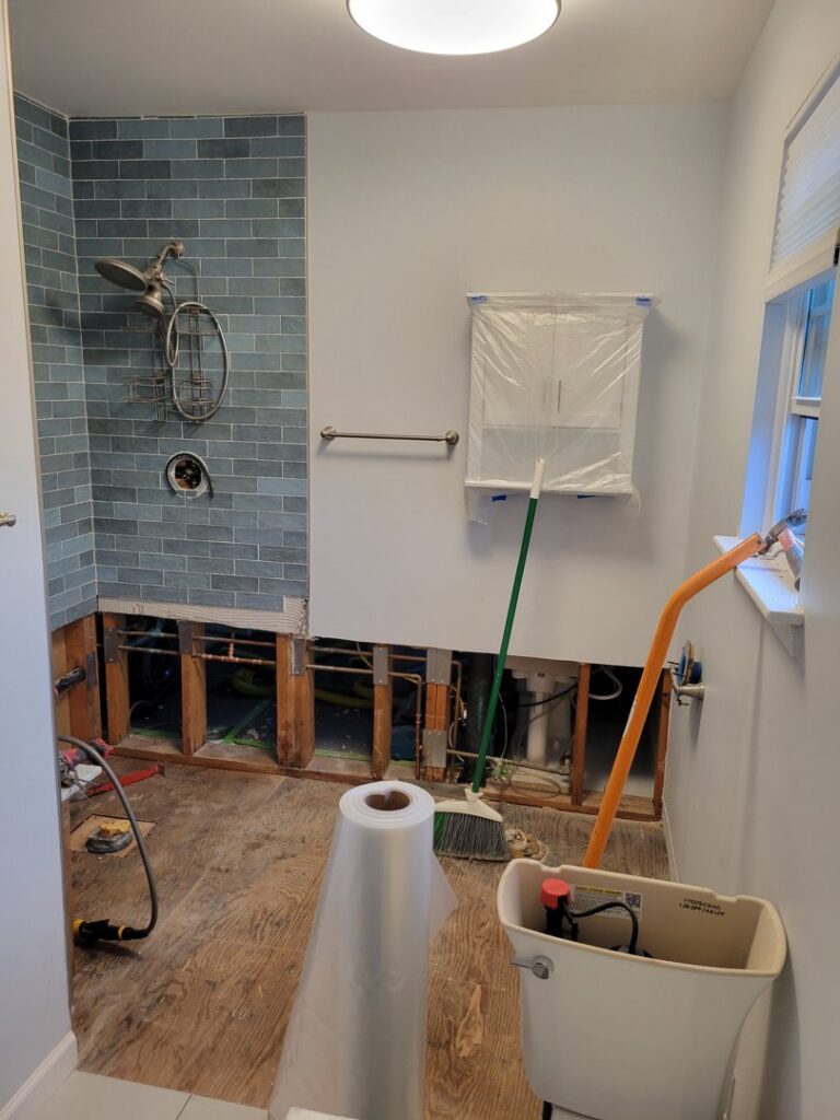 A bathroom undergoing water damage remediation with walls opened to expose studs and plumbing by New Method Restoration in Edison, NJ.