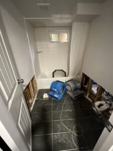 A bathroom undergoing water damage remediation, with walls removed to expose studs and industrial drying equipment in place, managed by Standard Restoration in Salt Lake City, UT.