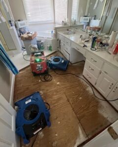 A bathroom undergoing water damage restoration with air movers and a dehumidifier on the exposed subfloor by Sentry Restoration in Volo, IL