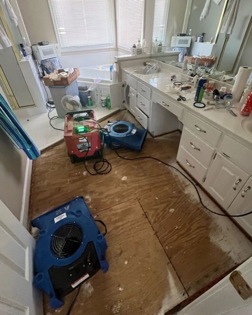 A bathroom undergoing water damage restoration with air movers and a dehumidifier on the exposed subfloor by Sentry Restoration in Volo, IL