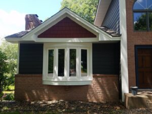 A house exterior showcasing a bay window with dark gray and red shake siding installed by Triton Exteriors in Maple Grove, MN.