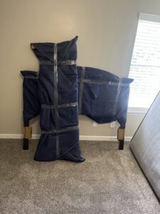 A bed frame and headboard carefully wrapped in moving blankets and tape for transport by Gifted Journey Movers in Gulfport, MS.