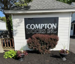 Two light beige carriage-style garage doors with windows and decorative hardware installed by Compton Doors, Inc. in Attleboro, MA