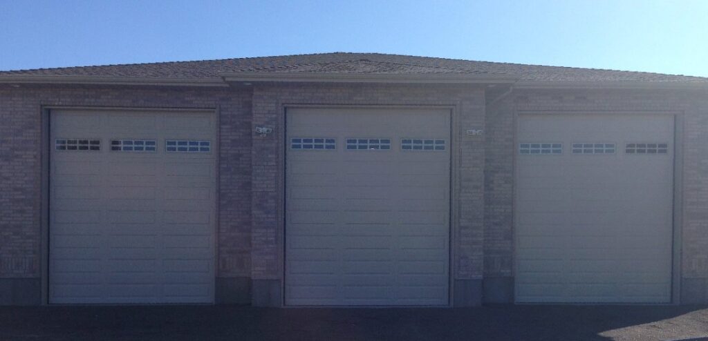 Three beige garage doors with top windows installed on a brick home by Wahlen Garage Doors in Ogden, UT