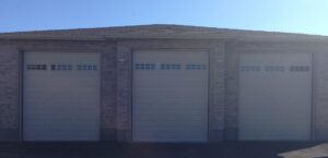 Three beige garage doors with top windows installed on a brick home by Wahlen Garage Doors in Ogden, UT