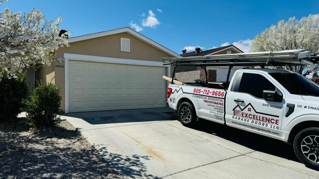 A beige panel garage door installed on a residential home by Excellence Garage Doors LLC in Albuquerque, NM, with their service truck visible.