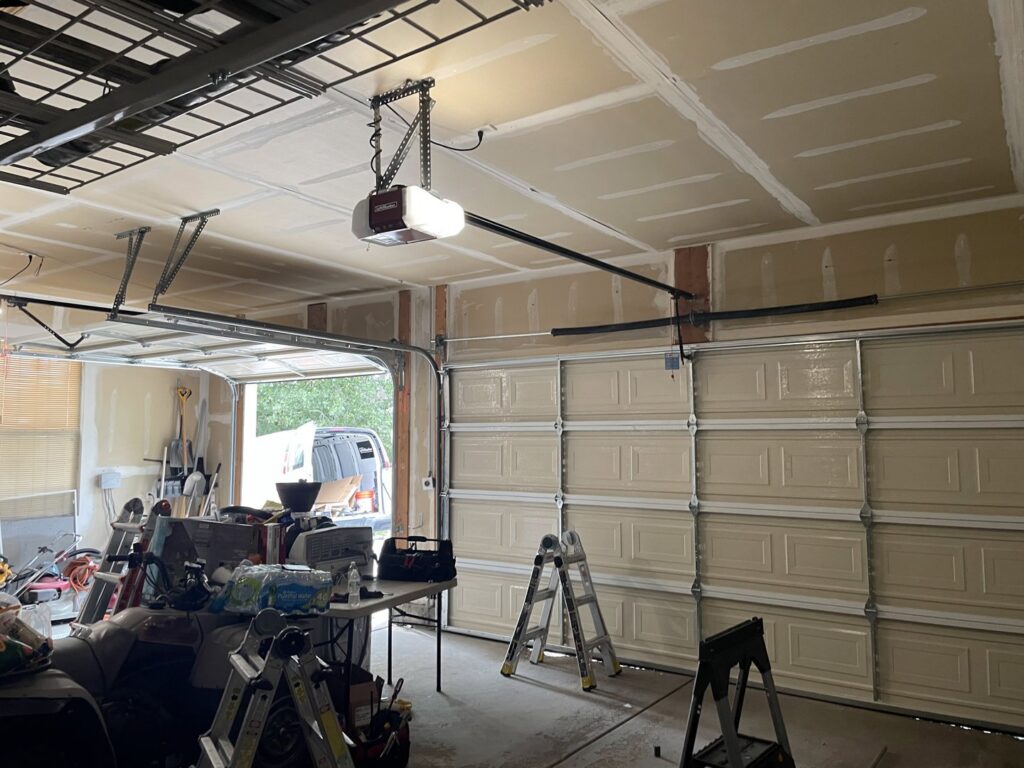 An interior view of a garage with a beige door and opener, ladders nearby, showing work by Delta Garage Door in Millcreek, UT.