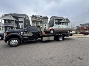 A beige sedan being towed on a flatbed truck by Black Mamba Towing & Recovery Llc in Aurora, CO.