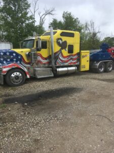 A Bevis Towing heavy-duty tow truck with an American flag design towing a white semi-truck in Cincinnati, OH.