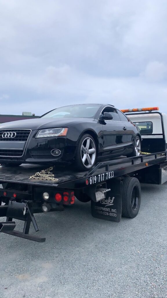 A black Audi coupe being transported on a flatbed tow truck by Cali kings Towing in San Diego, CA.