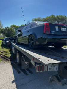 A black Cadillac sedan loaded onto a flatbed tow truck for transport by Heavy Hookz Towing in Fort Worth, TX.