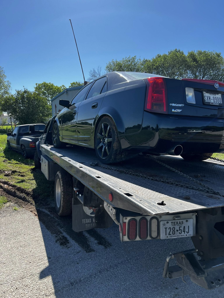 A black Cadillac sedan loaded onto a flatbed tow truck for transport by Heavy Hookz Towing in Fort Worth, TX.