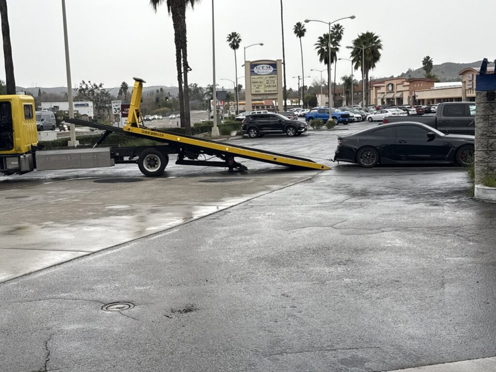 A black car being prepared for towing by a Ledesma's Towing truck in San Diego, CA.