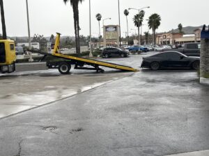 A black car being prepared for towing by a Ledesma's Towing truck in San Diego, CA.