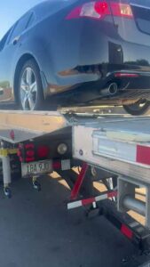 A black car being loaded onto a flatbed tow truck by Poly's Towing Glendale, AZ.