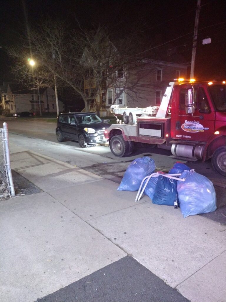 A black car being towed by a RonniesTowing&Recovery truck at night in Bryan, TX