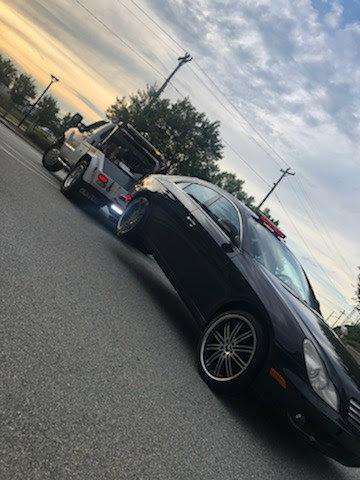 A black car being towed by a J & G Towing, LLC truck at sunset in Greensboro, NC.