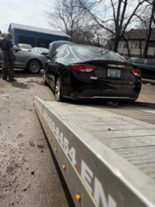A black car being loaded onto the ramp of a Tow & go flatbed tow truck in Louisville, KY.