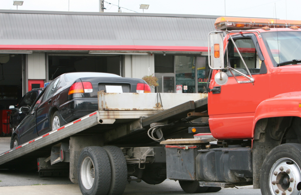 A black car being transported on a red flatbed tow truck by Bobby's TCB Towing in Detroit, MI