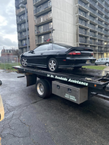 A black car being transported on a flatbed tow truck by Triple T's Tow, Tire, & Transportation in Cincinnati, OH.