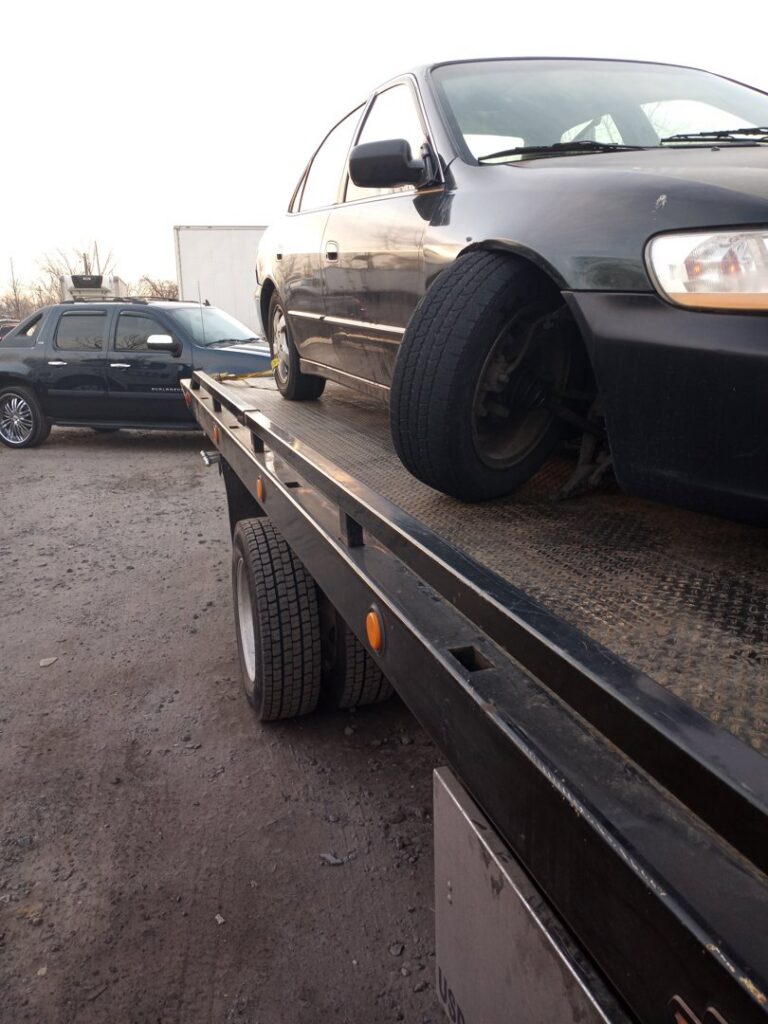 A black car being transported on a flatbed tow truck by Velez Towing in Newark, NJ.