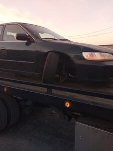 A black car being transported on a flatbed tow truck by Velez Towing, with a wider view of the scene in Newark, NJ.