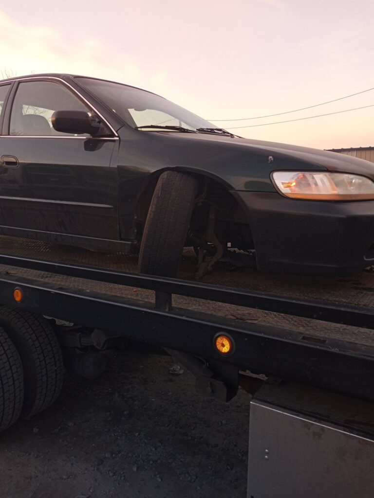 A black car being transported on a flatbed tow truck by Velez Towing, with a wider view of the scene in Newark, NJ.