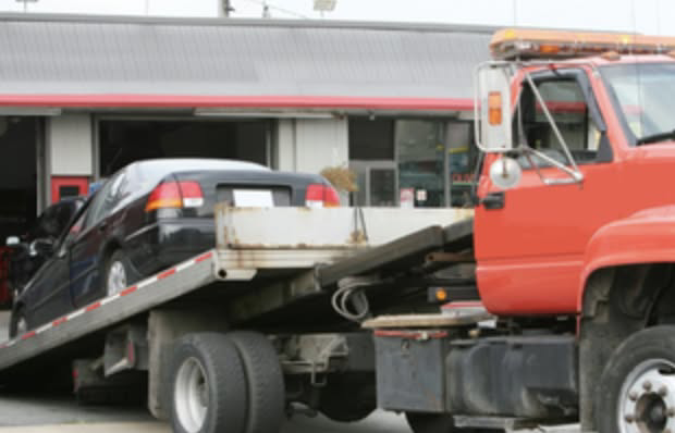A black car loaded onto a red flatbed tow truck, providing towing services by Bakersfield Towing Company in Bakersfield, CA.