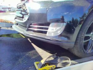A black car secured with straps on a flatbed tow truck by Ibanez Towing Service LLC in San Jose, CA.