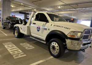 A black car being towed by a wrecker tow truck in a parking garage by Cali kings Towing in San Diego, CA.