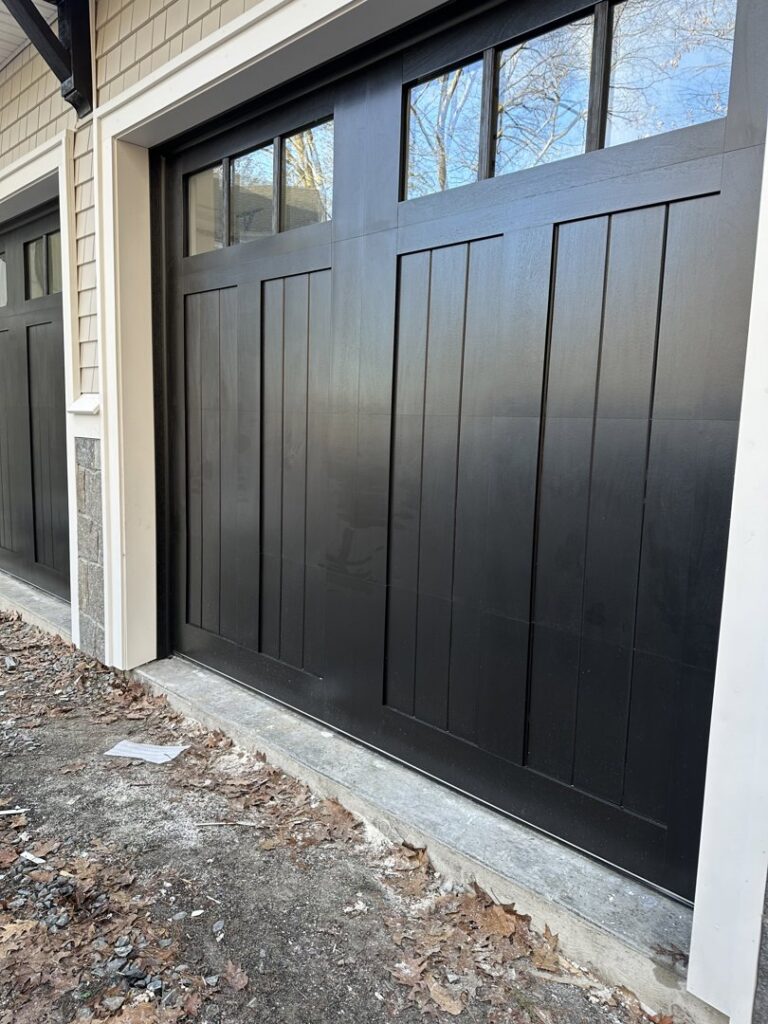 A close-up of a stylish black carriage-style garage door with top windows, installed by Steve Shumsky Unlimited Overhead Doors LLC in Hudson, NH