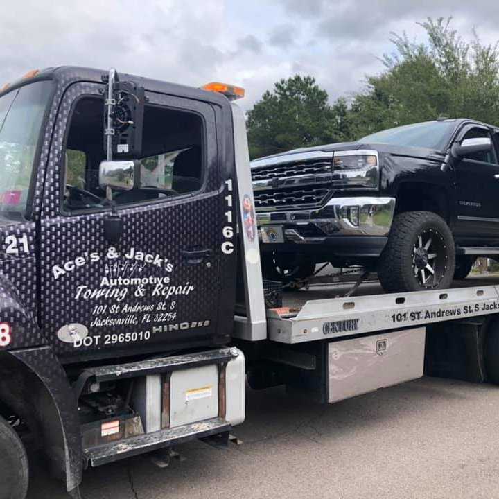 A black Chevrolet Silverado pickup truck being towed on a flatbed by Aces & Jacks Automotive in Jacksonville, FL.