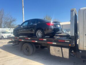 A black Chrysler 200 sedan being transported on a flatbed tow truck by Towing Near Me 247 LLC in Irving, TX.