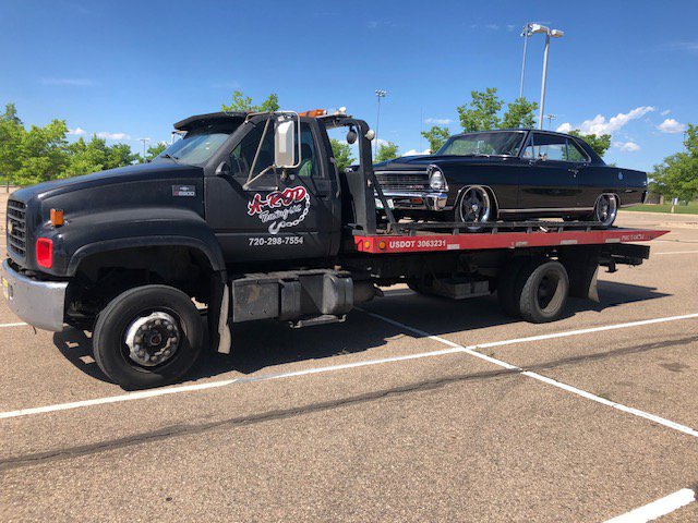 A black classic car being transported on a flatbed tow truck by A-ROD Towing in Denver, CO.