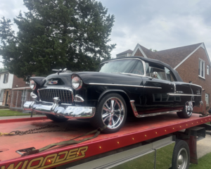 A black classic car, a Chevrolet Bel Air, secured on a flatbed tow truck by Triple D's Towing in Sterling Heights, MI.
