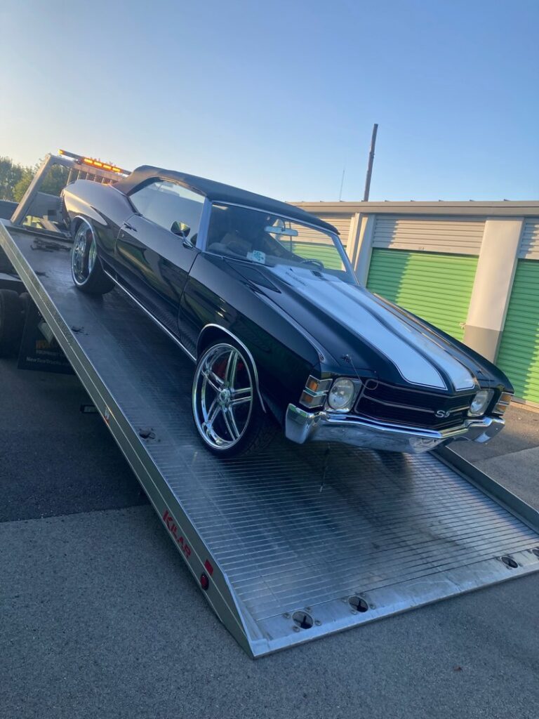 A black classic car with white racing stripes being loaded onto a flatbed tow truck by Towing Recovery Rebuilding Assistance Services in Naperville, IL