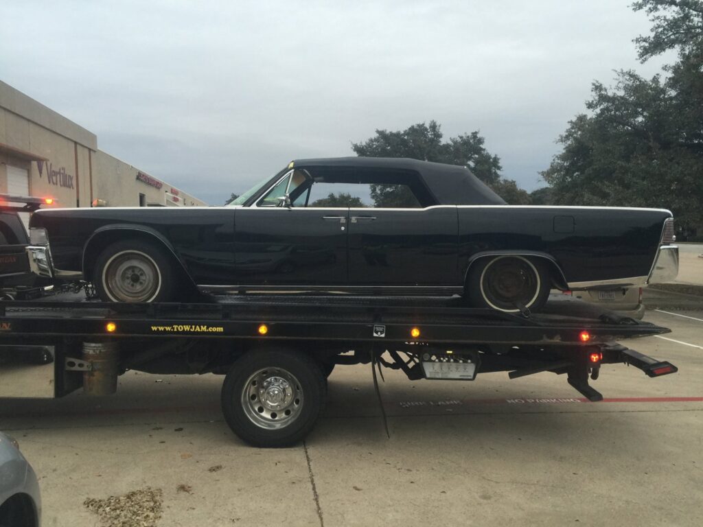 A black classic convertible car being transported on a Tow Jam flatbed tow truck in Dallas, TX.