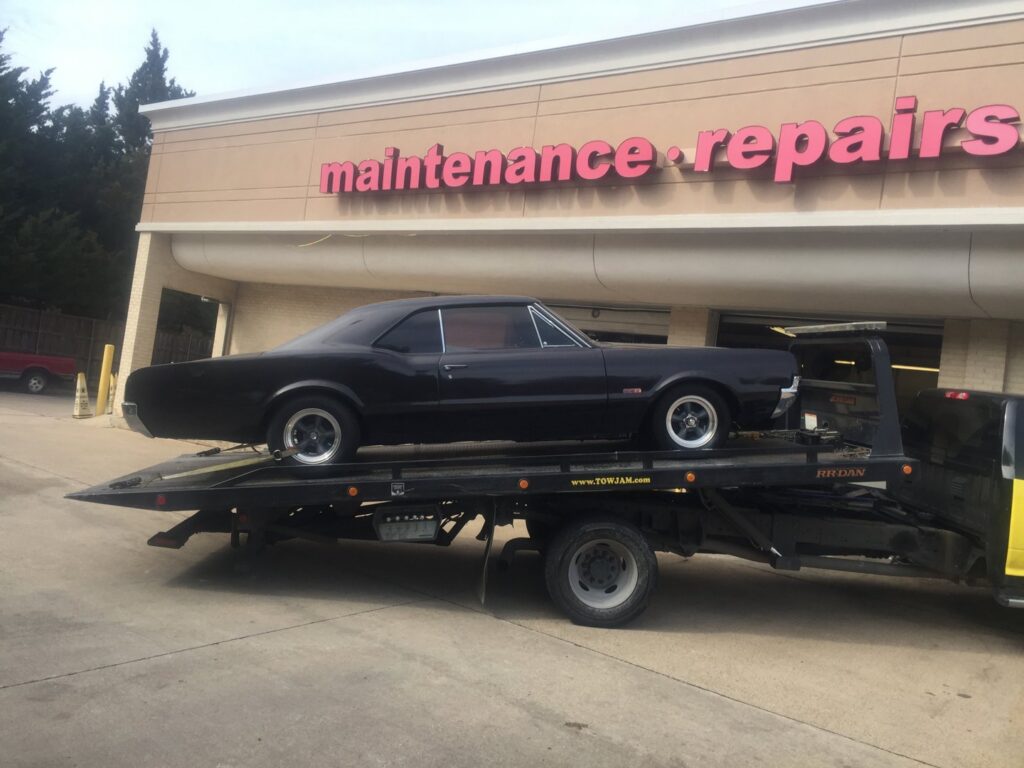 A black classic coupe car being delivered to a repair shop on a Tow Jam flatbed tow truck in Dallas, TX.