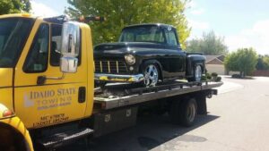 A black classic pickup truck being transported on a flatbed tow truck by Idaho State Towing and Recovery in Caldwell, ID.