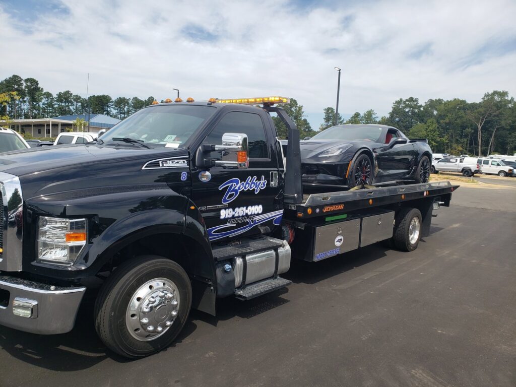 A black Corvette sports car loaded and secured on a Bobbys Towing & Recovery flatbed tow truck in Raleigh, NC.