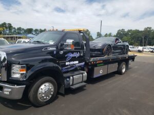 A black Corvette sports car loaded and secured on a Bobbys Towing & Recovery flatbed tow truck in Raleigh, NC.