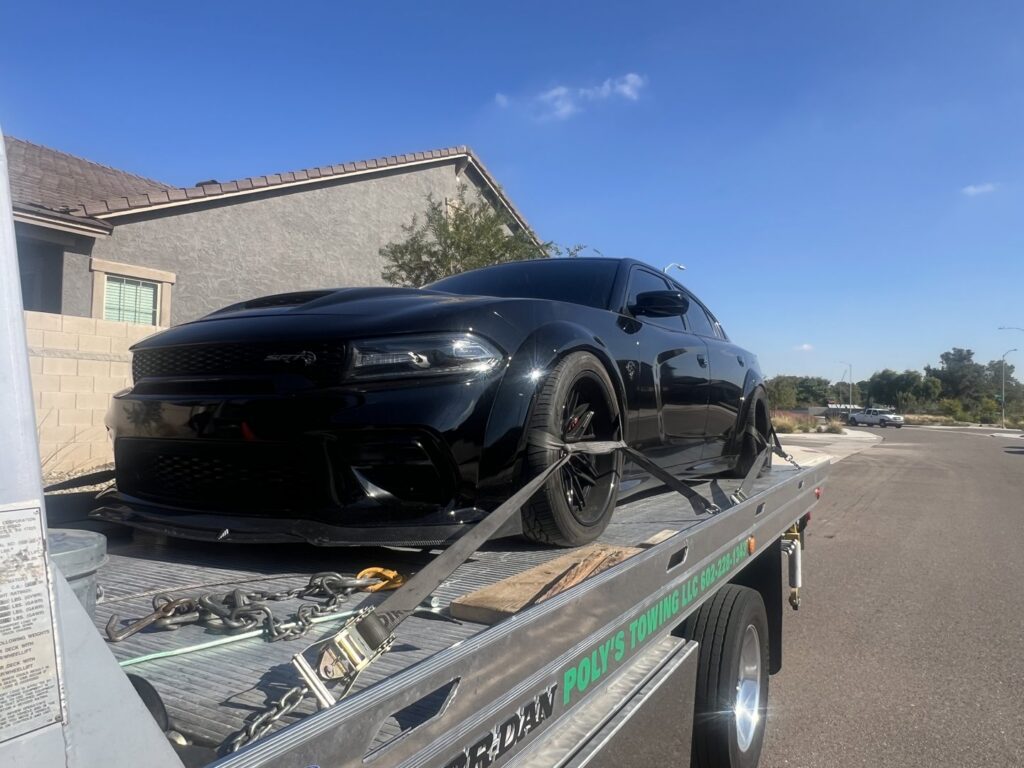 A black flatbed tow truck from Poly's Towing Glendale transporting a black Dodge Charger in Glendale, AZ.