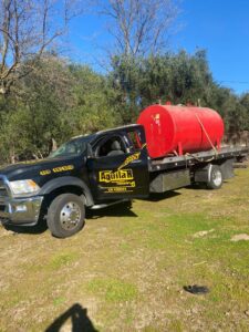 Aguilar Towing's black flatbed tow truck transporting a large red tank in San Jose, CA